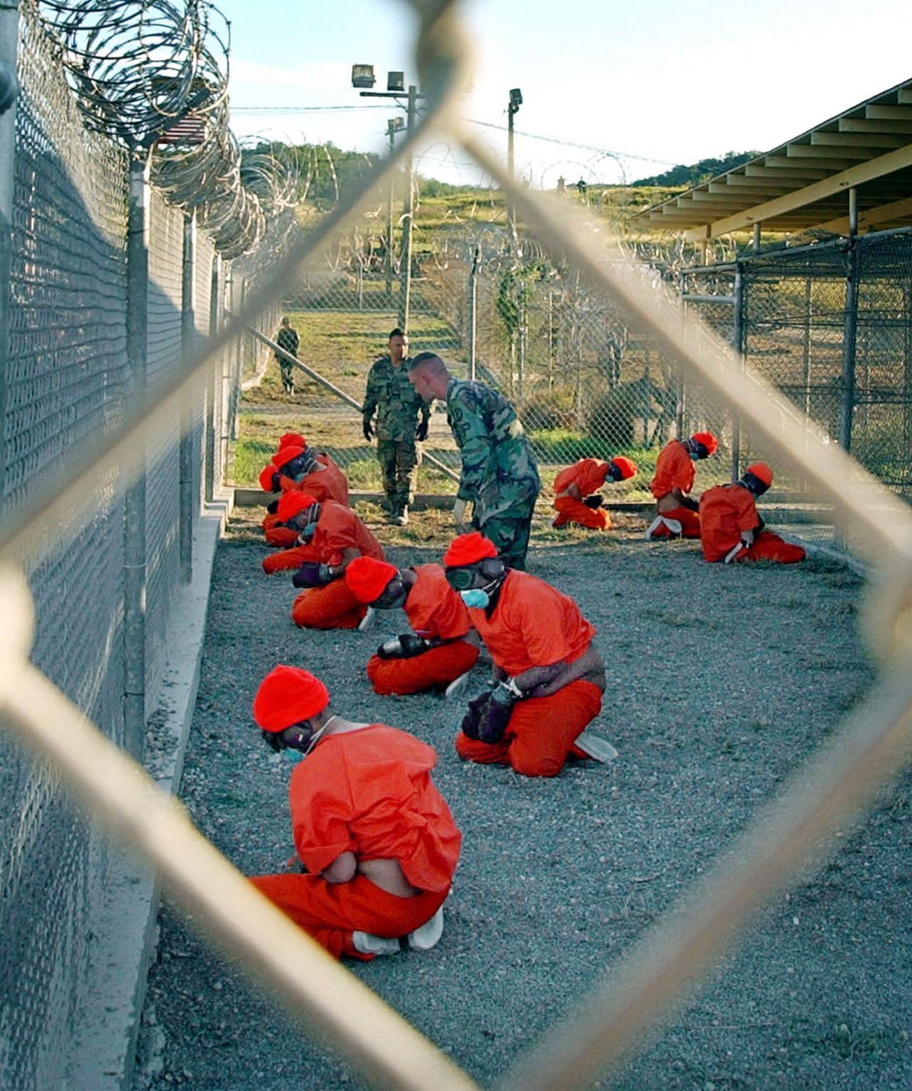 Häftlinge in orangefarbenen Overalls, die in einem Haftbereich unter den wachsamen Augen des Militärs im Camp X-Ray auf dem Marinestützpunkt Guantanamo Bay, Kuba, sitzen.