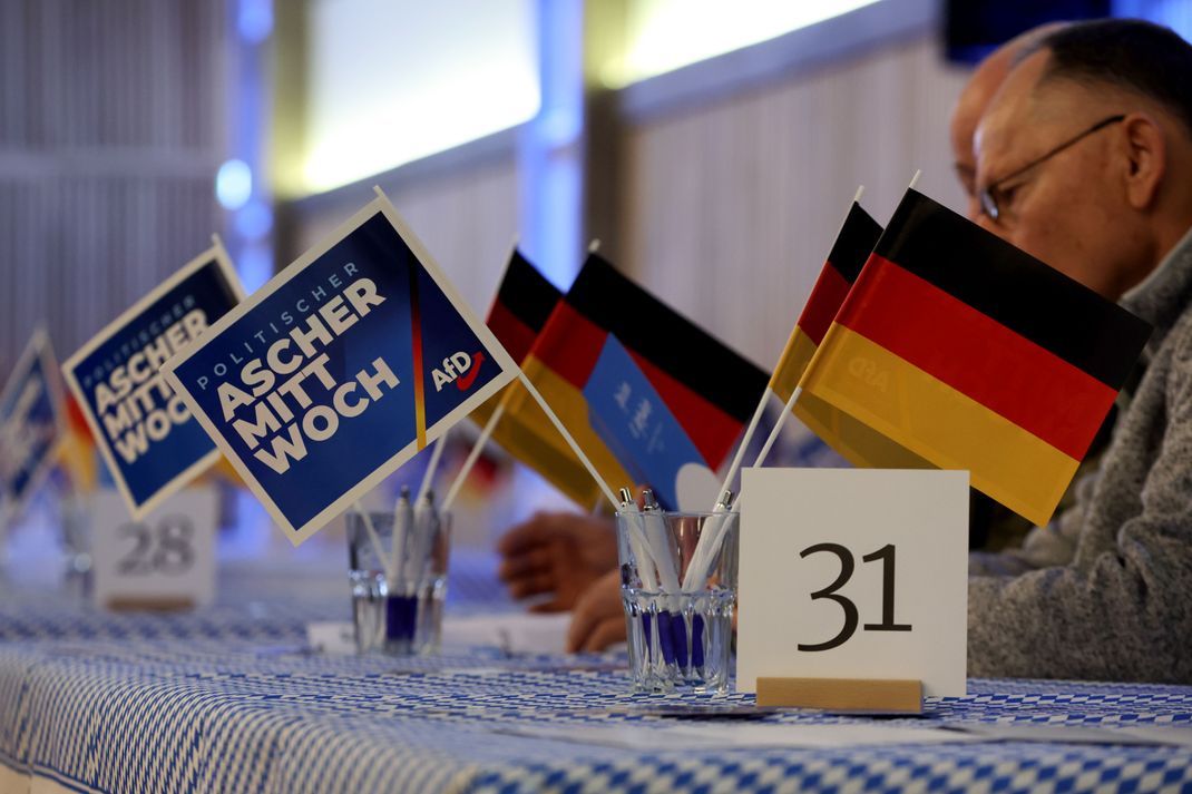 Politischer Aschermittwoch, AfD, im Donaucenter. Fähnchen mit der Aufschrift "Politischer Aschermittwoch" und dem Partei-Logo, sowie kleine Deutschland-Fahnen stehen auf einem Tisch.