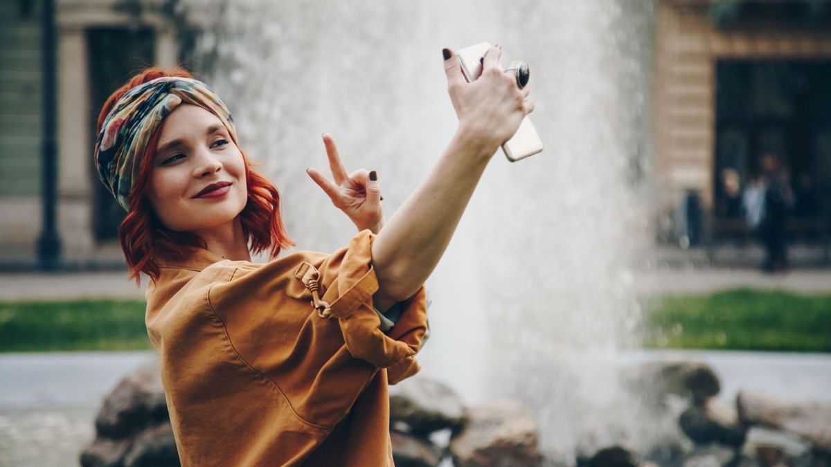 beautiful young woman taking selfie picture outdoors. hippie fashion blogger on vacation, taking self portrait with smartphone. street style, music festival portrait of authentic and fun young girl.