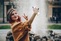 beautiful young woman taking selfie picture outdoors. hippie fashion blogger on vacation, taking self portrait with smartphone. street style, music festival portrait of authentic and fun young girl.