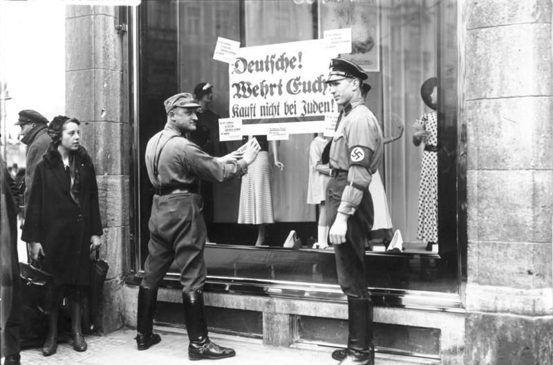 An den Fenstern jüdischer Geschäfte werden von Nationalsozialisten Plakate mit der Aufforderung "Deutsche, wehrt euch, kauft nicht bei Juden" angebracht.