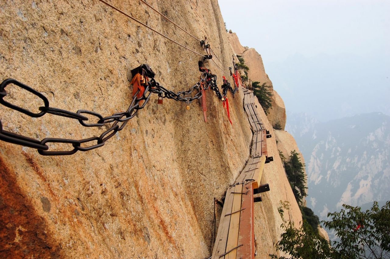 Mit 2.155 Metern ist der Huà Shān der höchste der fünf heiligen Berge Chinas. Das Gebirgsmassiv ist bekannt für seine steilen Felswände und gefährlichen Steige auf die Gipfel. Um zum Kloster zu gelangen, das hoch oben thront, muss man sich auf einem schmalen Pfad aus Holzplanken am Gestein entlang "schieben". Auf der einen Seite gibt eine Metallkette Halt, auf der anderen Seite tut sich der Abgrund auf.