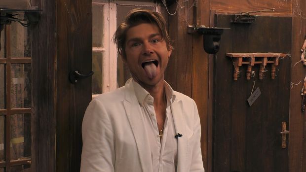 Jeremy Fragrance bei "Promi Big Brother" 2022 im weißen Anzug, streckt die Zunge raus.