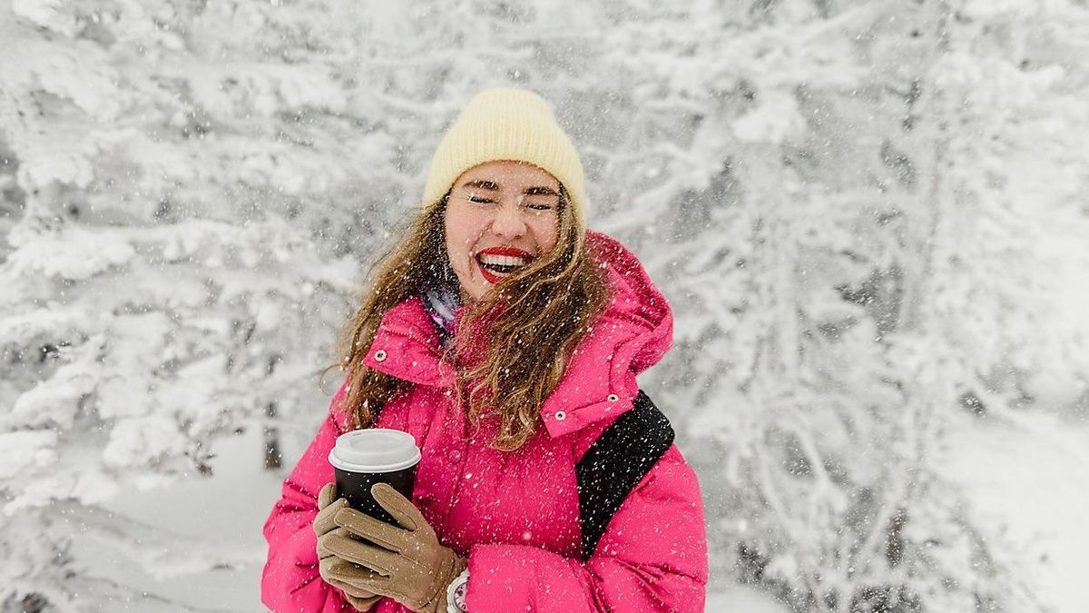 Cheerful woman with disposable coffee cup enjoying snowfall