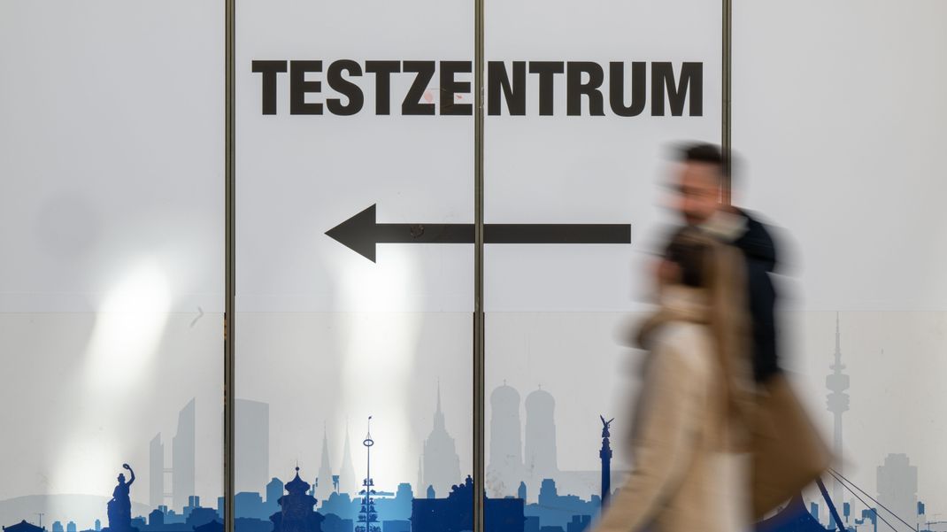 Passanten gehen in der Innenstadt an einem Corona-Testzentrum entlang.