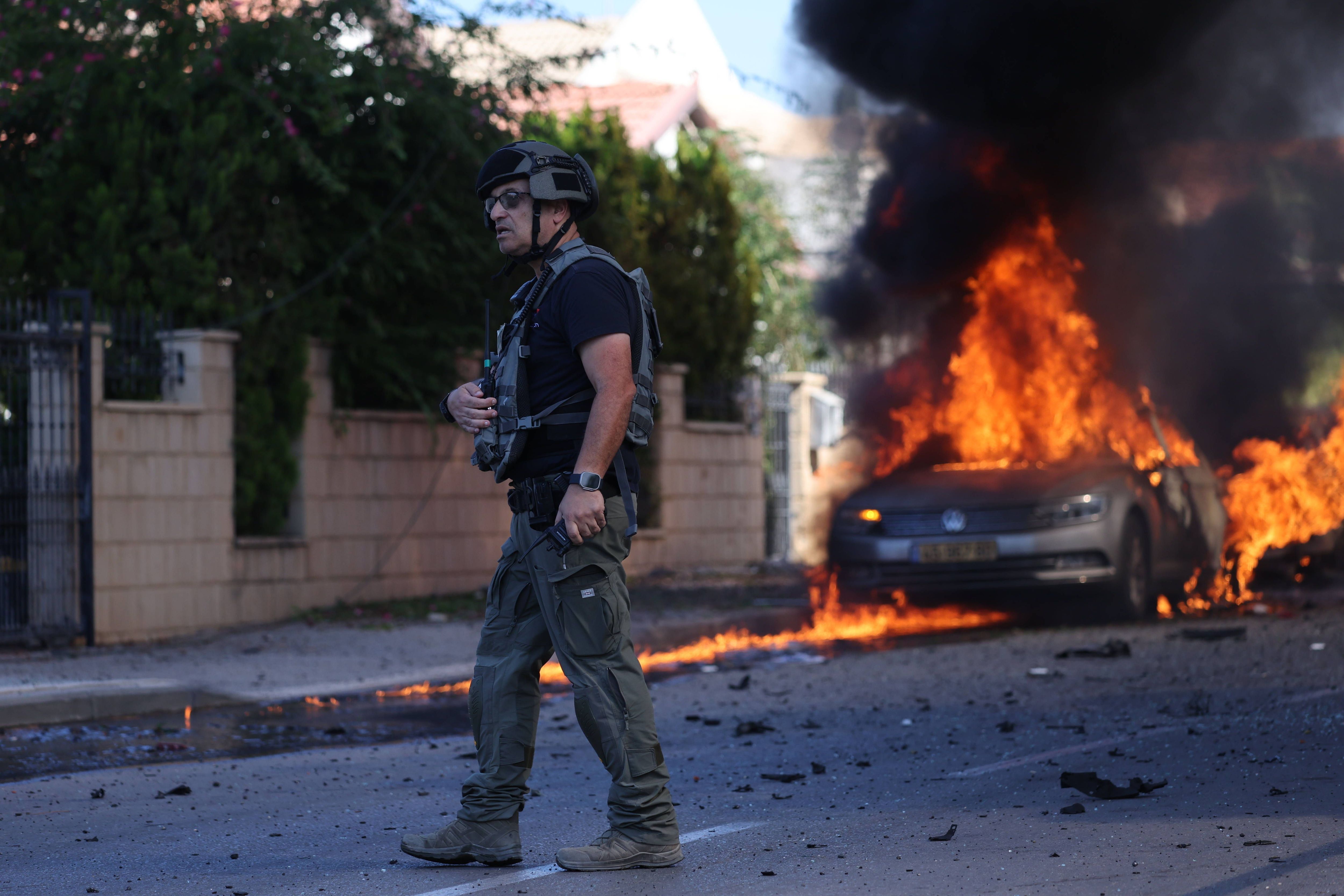 Ein israelischer Polizist steht vor einem brennenden Auto in Ashkelon.