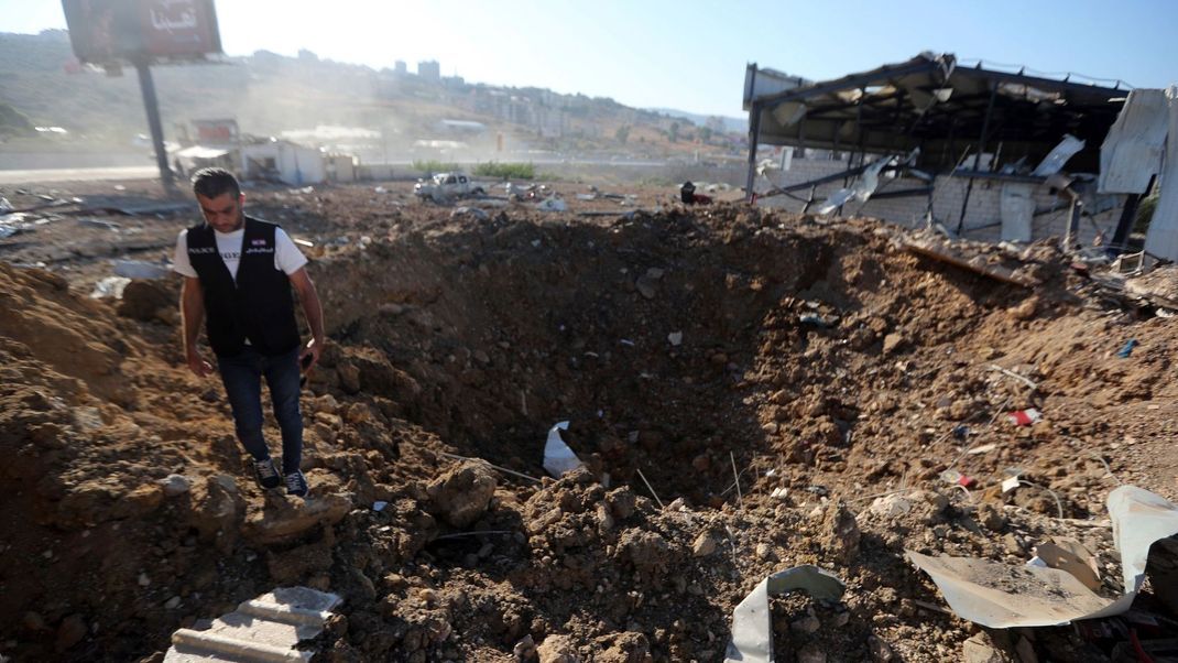 25. September 2024, Libanon: Ein libanesischer Polizist steht in der Nähe eines Kraters an der Stelle eines israelischen Luftangriffs, der einen Hangar in der südlichen Stadt Jiyeh getroffen hat.