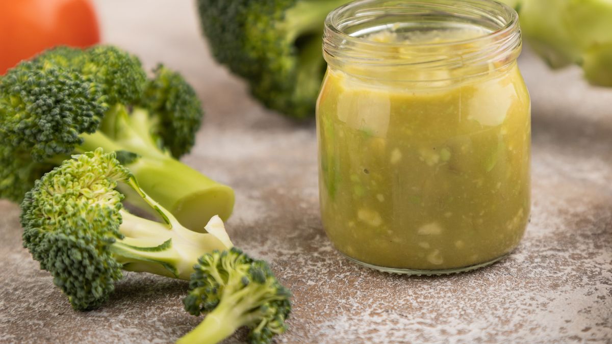 Baby puree with vegetable mix, broccoli, avocado in glass jar on brown concrete, side view, selective focus