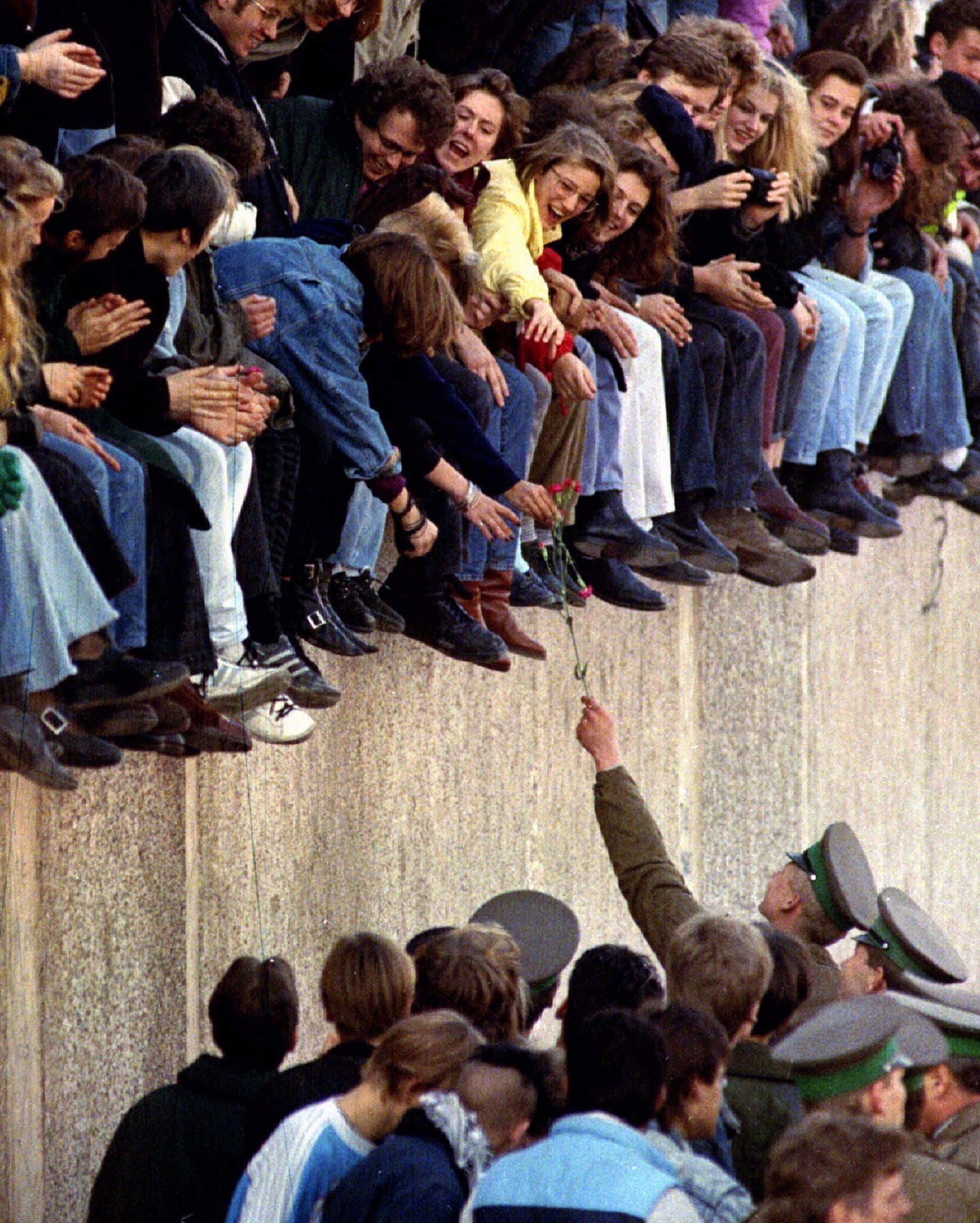 Ein ostdeutscher Grenzpolizist überreicht Westberlinern, die an der Berliner Mauer in der Nähe des Brandenburger Tors sitzen, am 10. November 1989 eine Blume.