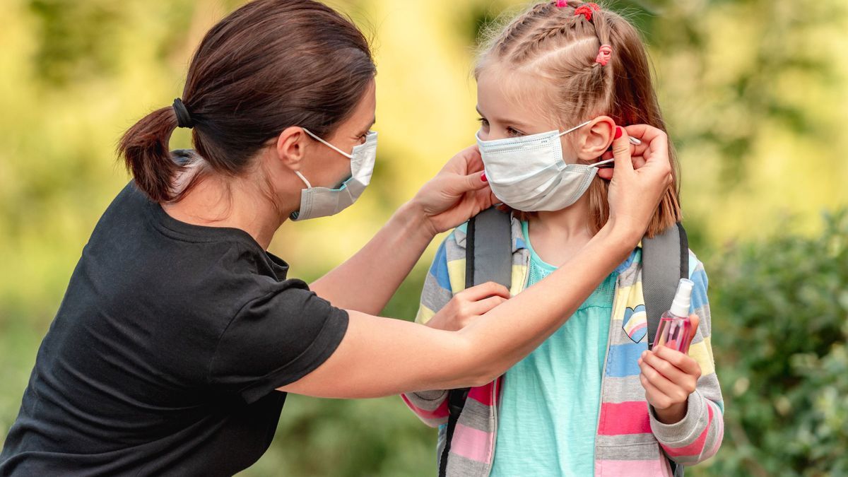 Mother putting mask on daughter before school