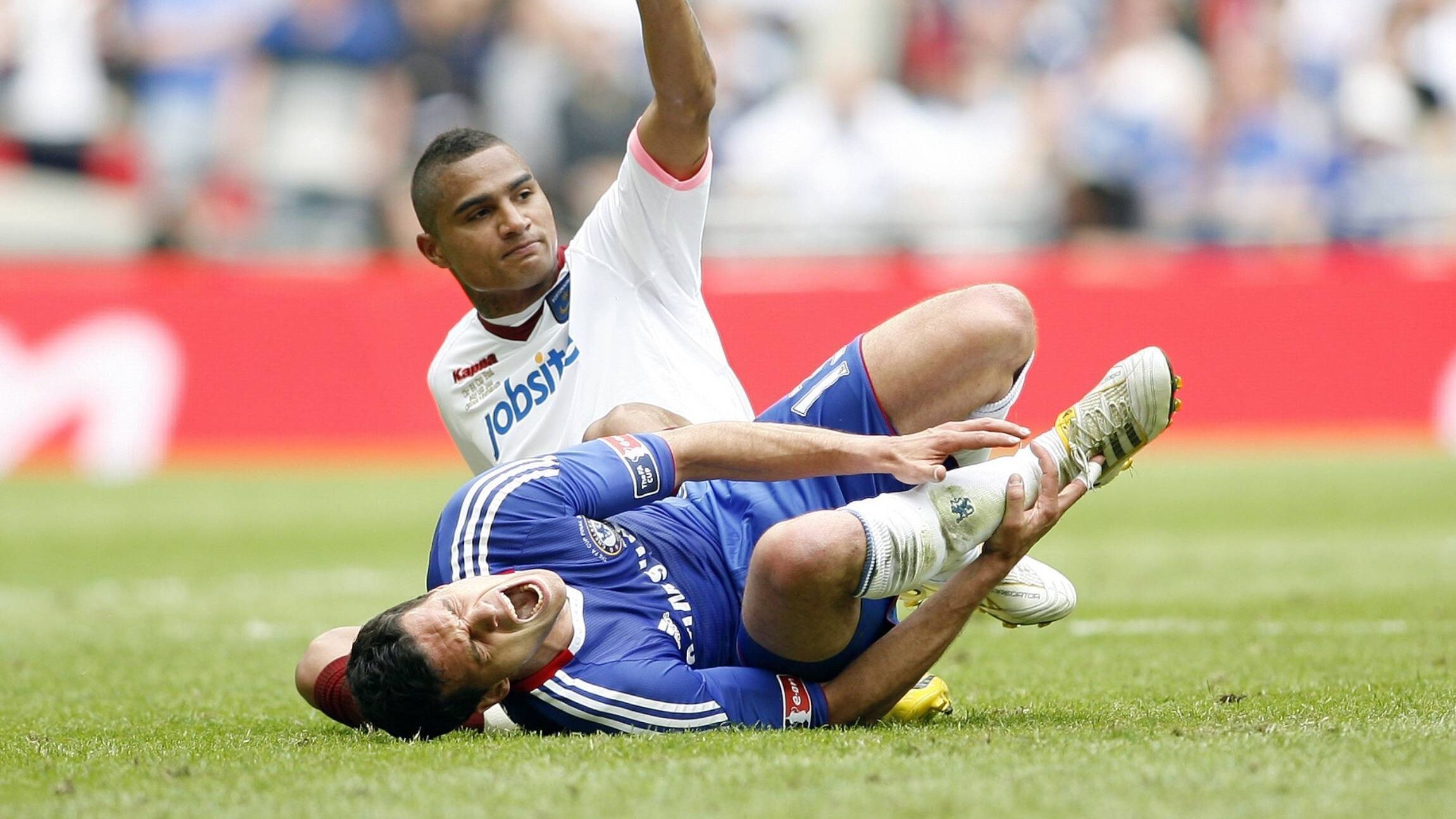 
                <strong>Im Chelsea-Trikot wird Ballack sogar zur Zielscheibe einer brutalen Attacke</strong><br>
                Die eine Demütigung reicht Chelsea aber nicht. Fast auf den Tag genau zwei Jahre später. Wembley-Stadion, FA-Cup-Finale, wieder mittendrin: Michael Ballack, wieder im blauen Chelsea-Trikot, wieder bringt ihm dieses Trikot Unheil. Diesmal trifft ihn der Schmerz früher, diesmal ist es ein physischer Schmerz. Anfang der zweiten Halbzeit tritt ihm Gegenspieler Kevin-Prince Boateng brutal auf den Knöchel. Für Ballack ist damit nicht nur das Spiel, sondern auch seine Länderspiel-Karriere vorbei. Bei der wenig später beginnenden WM in Südafrika verpasst Deutschland das Finale. Mit "Capitano" Ballack wären wir natürlich Weltmeister geworden! Aber er musste sich ja für Chelsea opfern. Den Sieg im Pokalfinale bejubelt übrigens Chelsea - ohne den verletzten Ballack.
              