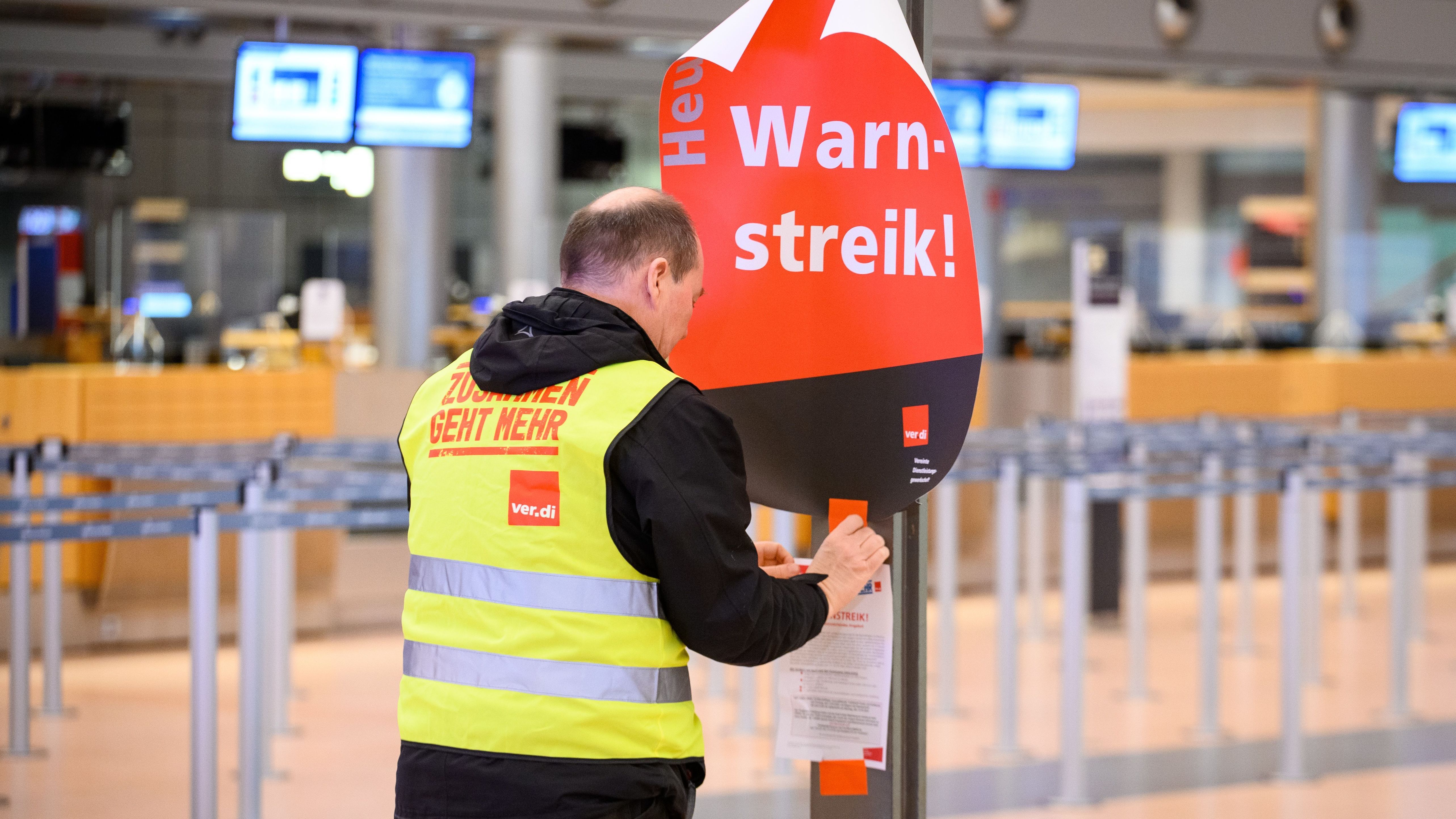 Ein Gewerkschaftsvertreter klebt in Hamburg ein Plakat mit der Aufschrift "Warnstreik!" und einen Flyer an die Anzeigetafel im leeren Terminal 2. 