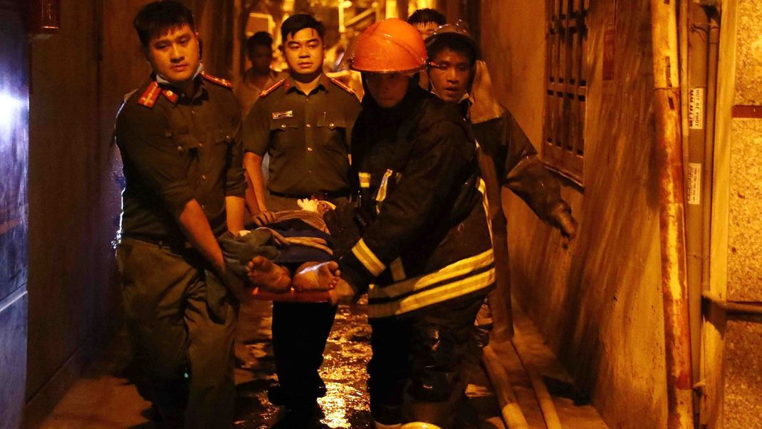 Rettungskräfte tragen eine Person auf einer Trage aus dem brennenden Gebäude in Hanoi. 