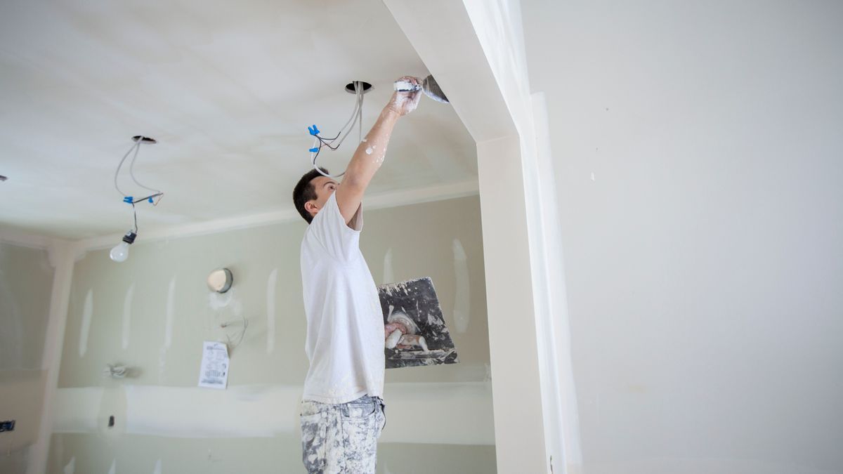 Tradesman plastering drywall with trowel in home