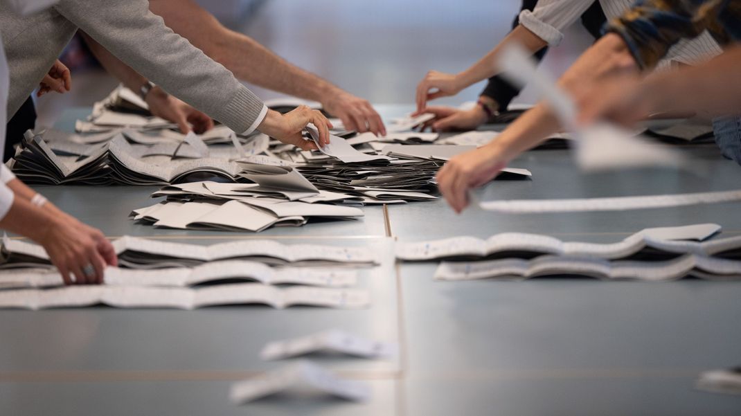 Wahlhelfer und Wahlhelferinnen zählen in einem Wahllokal Stimmzettel.