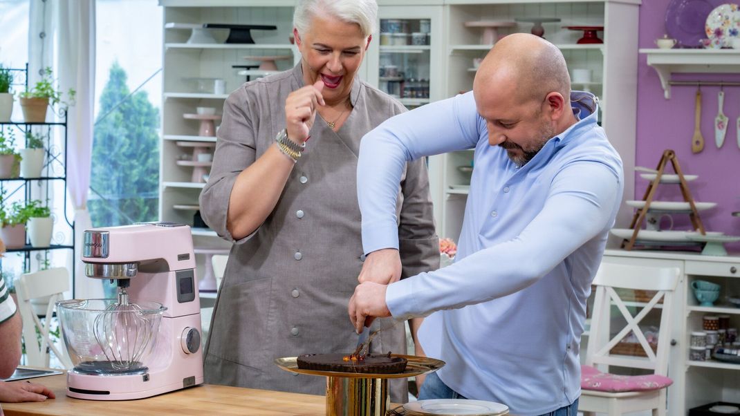 Bettina Schliephake-Burchardt und Christian Hümbs aus "Das große Backen" 2024 beim verzweifelten Versuch, eine Karamelltorte anzuschneiden.