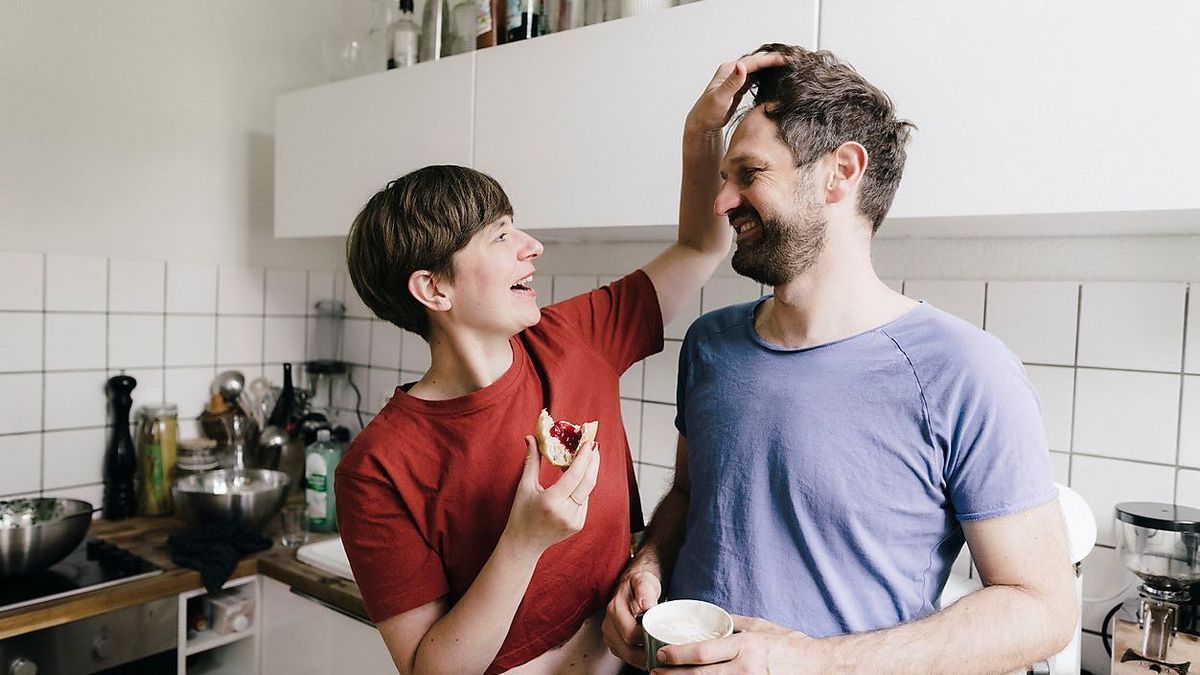 Woman caressing hair of man standing in kitchen at home