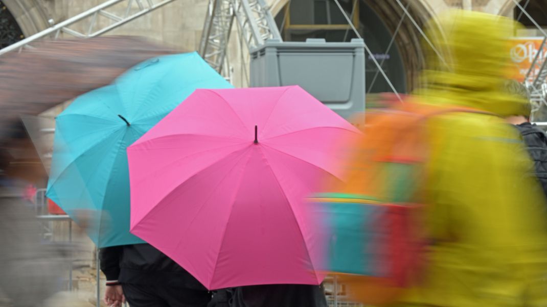 Passanten gehen mit Regenschirmen durch die Altstadt. 