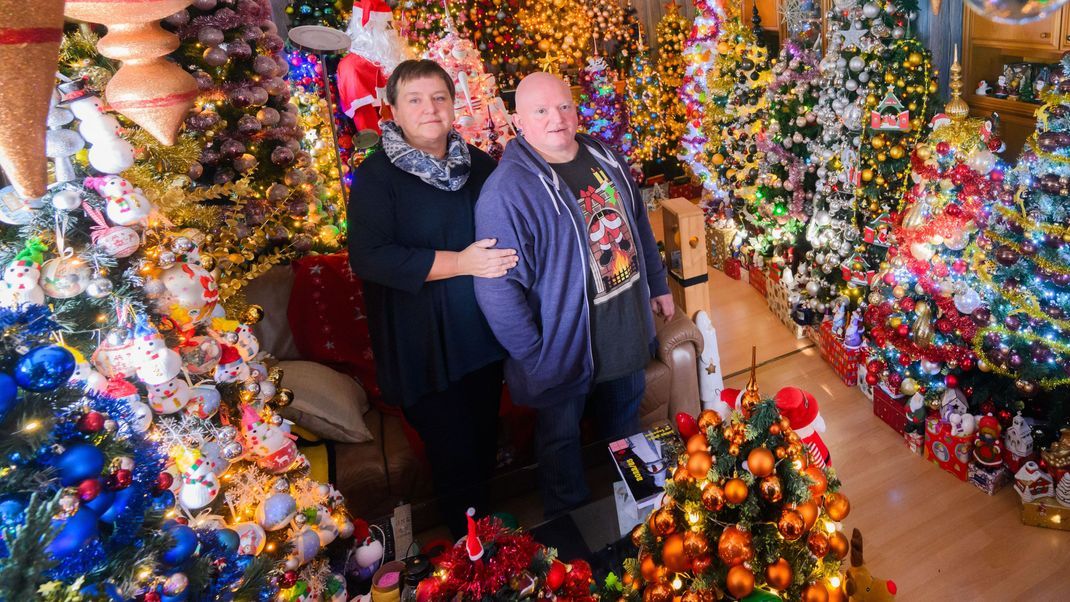 Weltrekord! Susanne und Thomas Jeromin stehen inmitten von 555 geschmückten Weihnachtsbäumen in ihrem Haus.