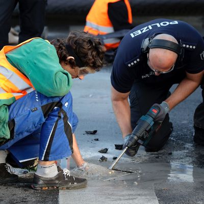 Ein Polizist entfernt mit einem Bohrer ein Teil Asphalt, um einen Aktivisten von der Straße zu lösen. (Archivbild)