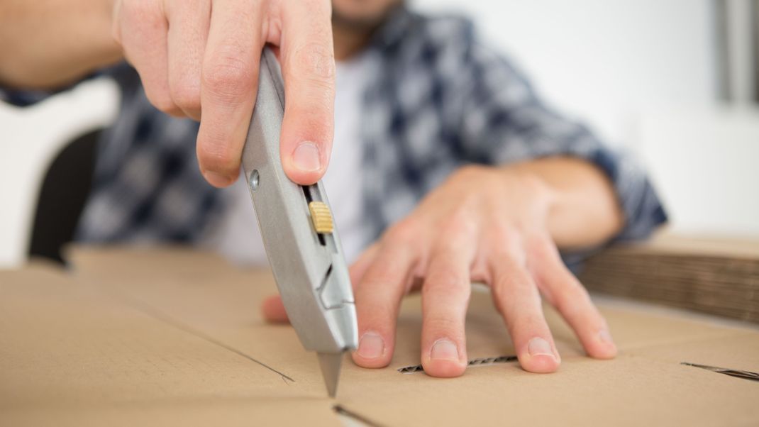 Mann benutzt säuberlich das Cuttermesser zum Schneiden von Karton